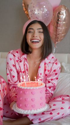 a woman sitting in bed with a pink cake and balloons