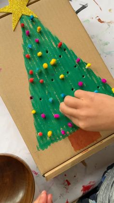 a child is painting a christmas tree on a cardboard box with sprinkles