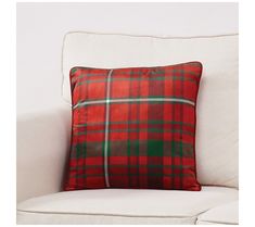 a red and green plaid pillow sitting on top of a white couch next to a wall