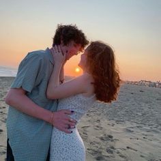 a man and woman kissing on the beach at sunset