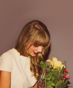 a woman holding a vase with flowers in it and looking down at the flower arrangement