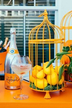 an orange table topped with lemons and a bird cage next to a bottle of booze