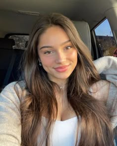 a woman sitting in the back seat of a car with long brown hair and wearing a white top