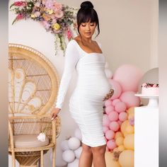 a pregnant woman in a white dress standing next to balloons and a chair with flowers on it