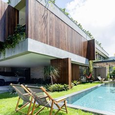 two lawn chairs sitting next to a swimming pool in front of a modern house with wooden sidings