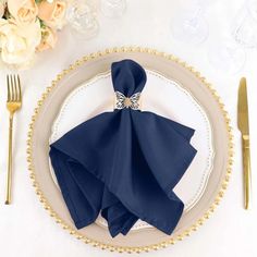 a place setting with blue napkins and gold cutlery on a white table cloth