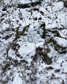 a sign that is on the ground in the snow with grass and rocks behind it