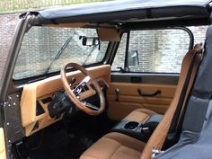 the interior of an old truck with leather seats and steering wheel, in front of a brick wall