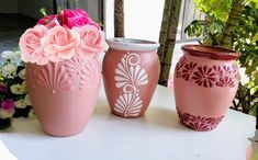 three pink vases sitting on top of a white table with flowers in the background