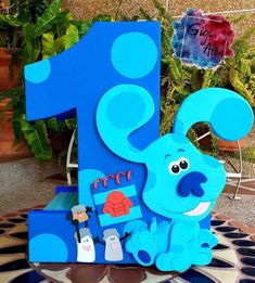 a blue number one shaped like a dog with people around it and plants in the background