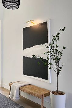 a painting hanging on the wall next to a wooden bench with a plant in it