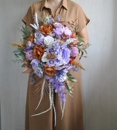 a woman wearing a brown shirt holding a purple and orange flower bouquet in her hands