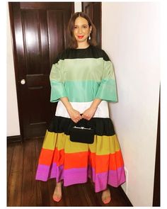 a woman standing in front of a door wearing a multicolored dress and carrying a black purse