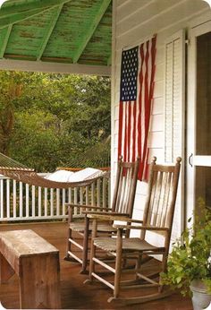 a wooden rocking chair on a porch with an american flag hanging from the ceiling above it