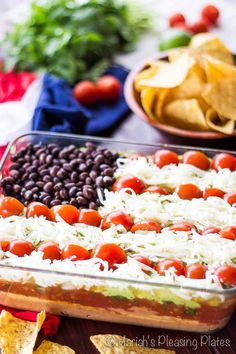 a casserole dish filled with black beans, tomatoes, cheese and tortilla chips