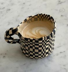 a black and white checkered cup sitting on top of a marble counter next to a spoon