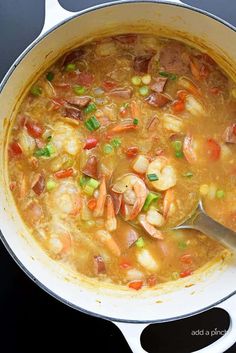 a pot filled with shrimp and vegetable soup on top of a stove next to a wooden spoon