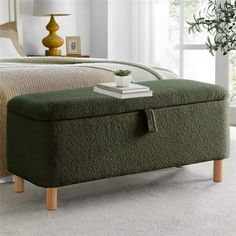 a bed with a green blanket on top of it and a wooden footstool