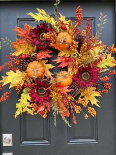 a wreath with pumpkins, leaves and berries hanging on a door