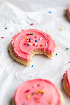 pink frosted doughnuts with sprinkles on top of white paper