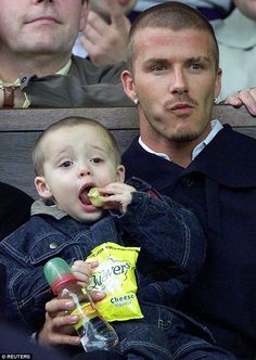 a young boy eating something while sitting next to an older man in the stands at a sporting event