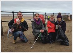 three adults and two children are sitting on the ground near a fence at the beach