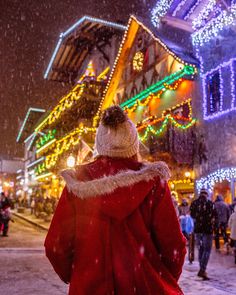 a woman in a red coat is walking down the street with christmas lights all around her