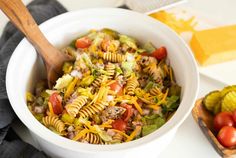 a white bowl filled with pasta salad next to a cutting board and wooden utensils