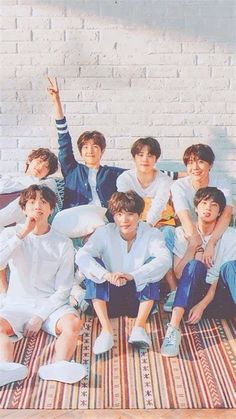 a group of young men sitting next to each other on top of a rug in front of a brick wall