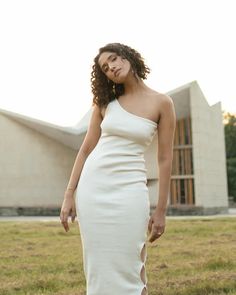 a woman standing in front of a building wearing a white dress with one side slit