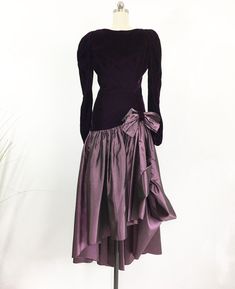 The perfect winter party dress! Long sleeve velvet deep purple bodice with a layered purple taffeta full skirt, adorned with a bow. The drop waist gives this dress a flapper feel. Asymetrical hemline, unlined, hidden zipper in the back. Deep V-back neckline. Gorgeous and ready for a fun night. DETAILS: Label: None Fabric: Velvet, Taffeta Lining: None Decade: 1980's MEASUREMENTS: Shoulders: 15'' Bust: 32'' Waist: 26'' Length: 48''front, 54''back Hips: 32'' Sleeves: 26'' Sleeve opening: 6'' widest Purple Evening Dress For Fall, Elegant Purple Winter Dresses, Purple Velvet Dress For Party, Purple Velvet Party Dress, Elegant Purple Velvet Dress, Formal Purple Velvet Dress, High Low Cocktail Dress, Columbia Tn, Country Dresses