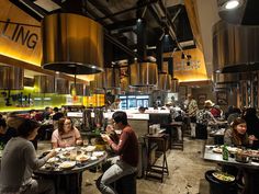 people sitting at tables in a restaurant with food on the table and hanging lights above them