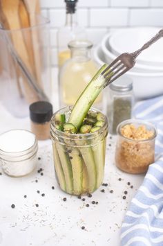 a jar filled with cucumbers sitting on top of a table next to bowls and utensils