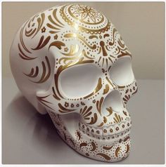 a white and gold skull with intricate designs on it's face, sitting on a table