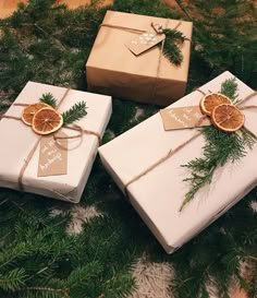 three wrapped presents sitting on top of a table covered in pine branches and orange slices