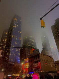 a city street at night with traffic lights and tall buildings in the foggy sky