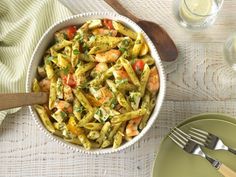 a white bowl filled with pasta and shrimp next to a glass of water on top of a table