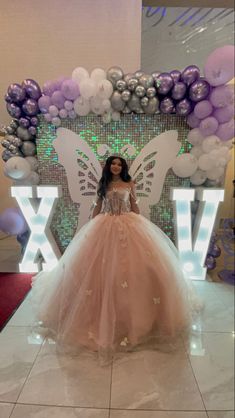 a woman in a ball gown standing next to a giant balloon arch with the letter v on it