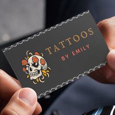 a person holding up a business card that says tattoos by emily with a skull on it