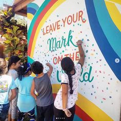 children are writing on the side of a colorful wall that says leave your mark on the world