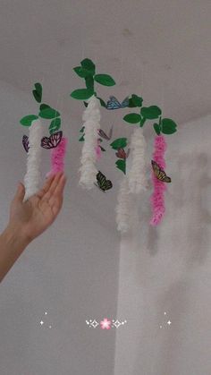 a hand is reaching up to some paper flowers and butterflies hanging from the ceiling in a room