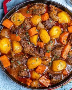 beef stew with carrots, potatoes and parsley in a red pot on a blue towel