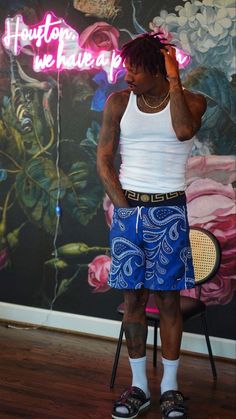 a man standing in front of a wall with flowers painted on it and holding a tennis racquet