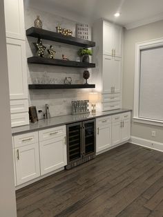 an empty kitchen with white cabinets and wood flooring is pictured in this image, there are shelves on the wall