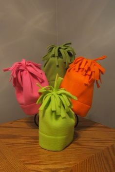 four hats are sitting on top of a wooden table and one is pink, green, orange, and yellow