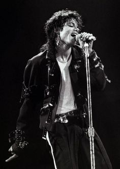 michael jackson performing on stage with his microphone up to his ear and wearing all black