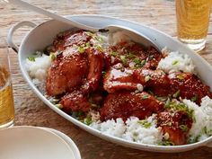 there is meat and rice in the dish on the table next to two glasses of beer