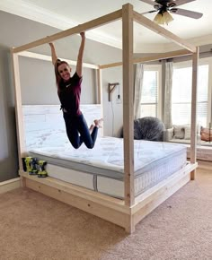 a woman jumping in the air on top of a bed with a wooden frame and mattress