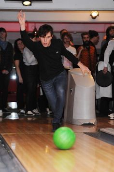 a man is bowling down a bowling alley with his arms in the air as people look on