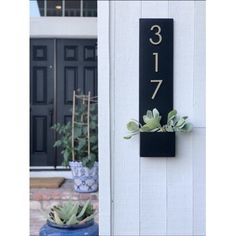 a house number sign mounted to the side of a white wall with succulents